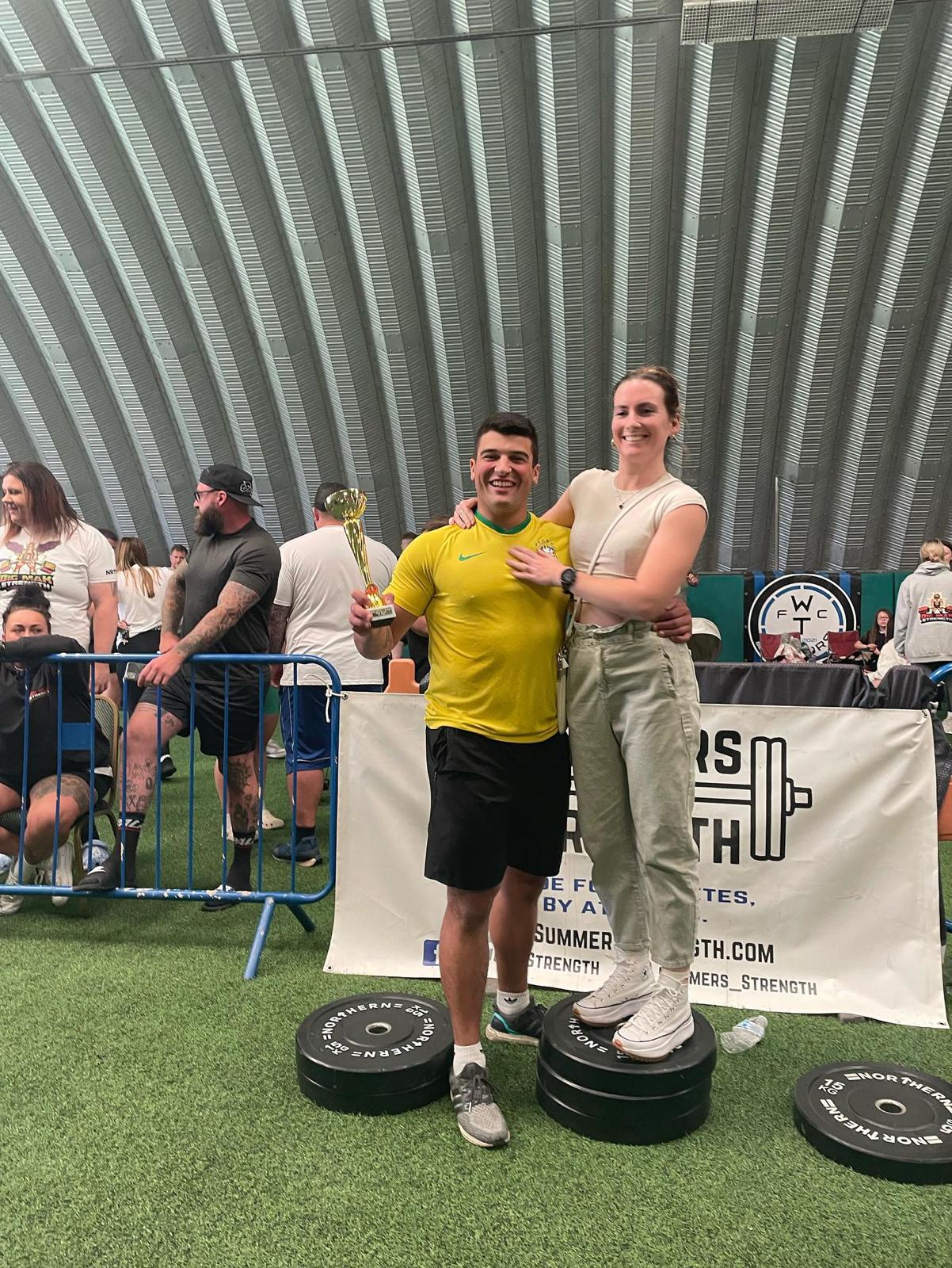 Mario Portela at a strength competition holding a trophy, next to his partner